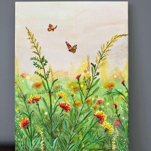 May include: A vibrant painting of a wildflower meadow with two orange butterflies fluttering above. The artwork features a mix of yellow, red, and green plants, creating a lively and colorful scene. The canvas is rectangular and set against a neutral background.