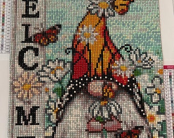 Könnte beinhalten: Diamantmalerei eines Willkommensschildes mit einem Schmetterlings- und Blumendesign. Das Wort "WELCOME" ist vertikal auf der linken Seite dargestellt. Das Kunstwerk zeigt einen Schmetterling mit orangefarbenen, roten und gelben Flügeln, umgeben von weißen Blumen.