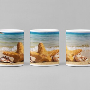 以下が含まれることがあります： ビーチのシーンがプリントされた白いセラミック製のマグカップが3つ。シーンは、青い海の砂浜に、ヒトデと貝殻が2つある様子を描いています。
