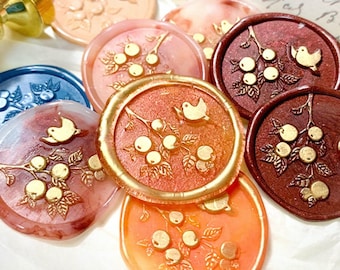 Può includere: Assortimento di sigilli di cera con un designo di uccello e bacche. I sigilli sono di vari colori, tra cui rosso, arancione, blu e bianco.