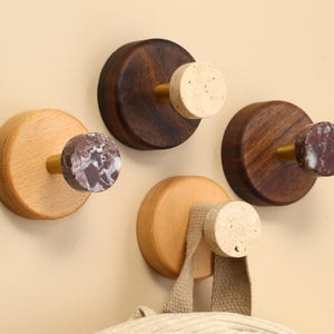 May include: A selection of wooden wall hooks in different finishes. Some are light wood, others are dark brown. The knobs have marble, cork, and wood grain patterns. A beige bag hangs from one hook.