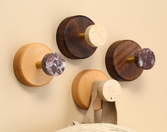 May include: Four wooden wall hooks with decorative knobs. Two hooks are made of light wood, and two are dark wood. The knobs are made of cork and marble. A beige bag hangs from one hook.