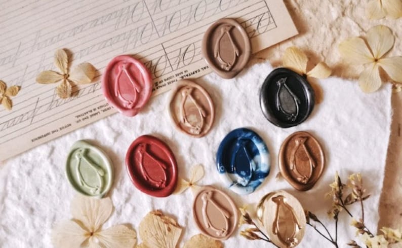 May include: Assortment of ten wax seals featuring a penguin design. The seals are in various colors, including red, blue, green, gold, and silver.