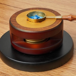 May include: A wooden wax seal kit with a brass melting pot and a wooden handle. The kit is on a black wooden base.