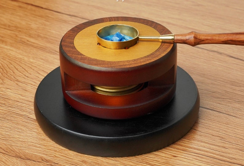 May include: A wooden wax seal kit with a brass melting pot and a wooden handle. The kit is on a black wooden base.