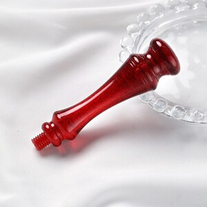 Puede incluir: Un tap&oacute;n de botella de vidrio rojo con un extremo roscado. El tap&oacute;n tiene un acabado brillante ligeramente brillante.