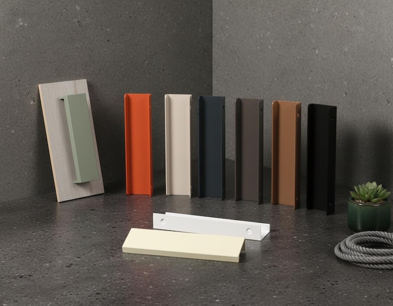 May include: A selection of cabinet pulls in a range of colours: green, orange, cream, navy, brown, and black. Some are mounted on a wooden board. Additional pulls are laid flat. A small potted plant and a rope are also present.