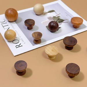 Puede incluir: Una colección de pomos y tiradores esféricos de madera en varios tonos de marrón y tonos de madera natural. Algunos pomos son redondos, otros cilíndricos y algunos tienen una superficie texturizada.