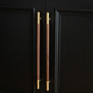 Peut inclure: Gros plan sur une armoire noire avec deux poignées de barre en bois et en laiton. Les poignées sont verticales, avec un centre en bois foncé et des extrémités en laiton. Les portes de l'armoire sont noires avec des panneaux encastrés.