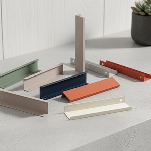 May include: A selection of colourful metal cabinet pulls in shades of green, pink, navy, and orange. The pulls have a modern, minimalist design, with a simple L-shape. Some are upright, while others are lying flat. Each pull has a hole for mounting.