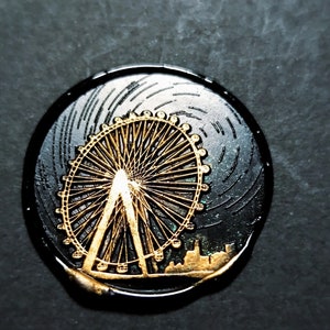 K&ouml;nnte beinhalten: Ein schwarzes und goldenes rundes Wachssiegel mit einem detaillierten Design eines Riesenrads. Das Riesenrad ist in Gold umrandet und hat einen schwarzen Hintergrund.