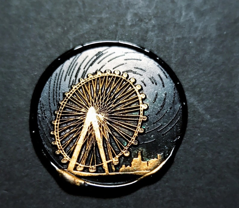 K&ouml;nnte beinhalten: Ein schwarzes und goldenes rundes Wachssiegel mit einem detaillierten Design eines Riesenrads. Das Riesenrad ist in Gold umrandet und hat einen schwarzen Hintergrund.