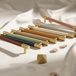 May include: A collection of cabinet pulls in various colors, including brown, blue, green, and beige, with gold-toned cylindrical ends. The pulls are arranged on a white surface, suggesting a home decor theme.