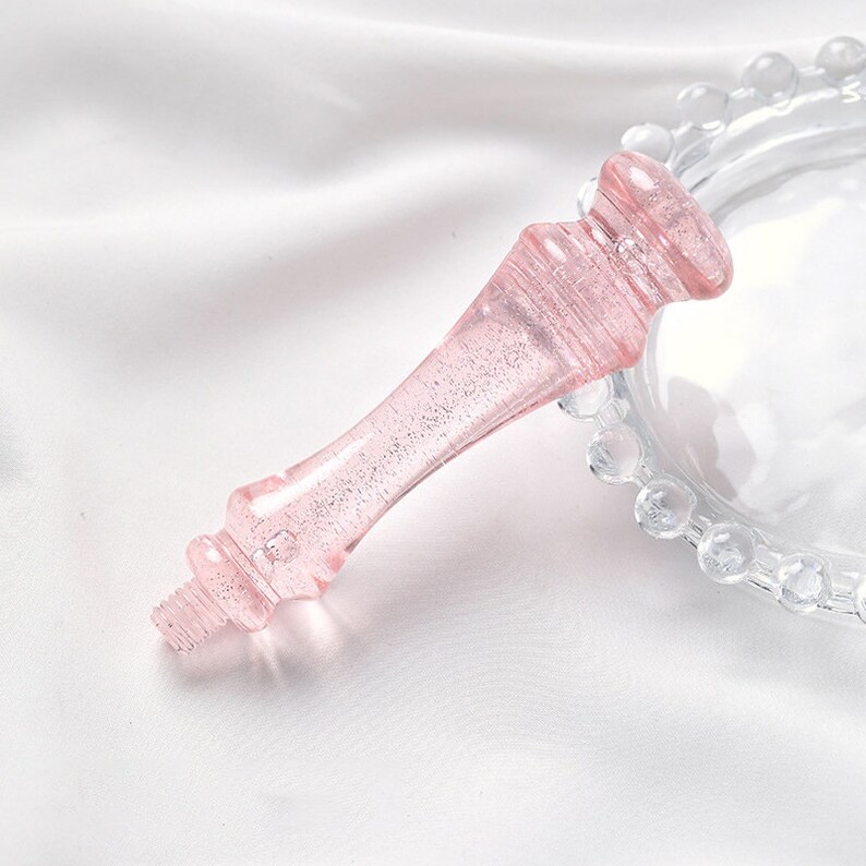 Puede incluir: Un mango de soporte para pastel de vidrio rosa con un acabado brillante. El mango tiene forma de corona y tiene un dise&ntilde;o decorativo.