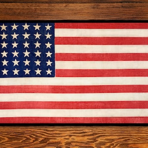 May include: A vintage-style American flag with 48 stars on a blue field and 13 red and white stripes. The flag is framed in black and displayed against a wood background.
