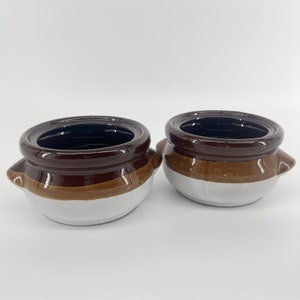 May include: Two brown and white ceramic soup bowls with rounded edges and small handles. The bowls have a brown glaze on the top and a white glaze on the bottom.