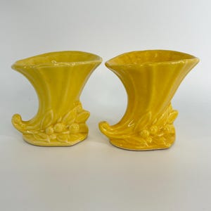 May include: A pair of yellow ceramic cornucopia vases with leaf and berry details.
