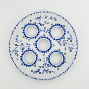 May include: A white ceramic egg holder with a blue floral design and five holes for eggs.