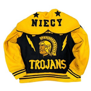 May include: A yellow and black varsity jacket with the word "NIECY" on the back, a black and gold Trojan head logo, and the word "TROJANS" below it.