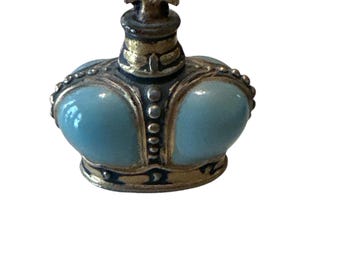 May include: A small, blue and gold crown-shaped bottle stopper. The crown has a cross on top and is decorated with gold trim and small beads.
