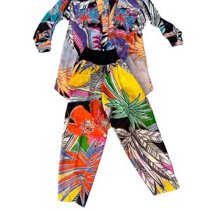 May include: A colorful two-piece outfit with a long-sleeved button-down shirt and matching pants. The shirt and pants feature a tropical print with flowers, leaves, and geometric patterns in shades of blue, green, orange, pink, and yellow.