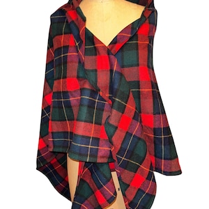 May include: A red, green, and blue plaid cape draped over a mannequin. The cape features a hood and a ruffled front, showcasing a classic tartan pattern. The fabric is a medium weight, suitable for cooler weather.