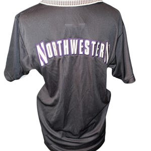 May include: Black short-sleeved polo shirt with a white collar and the word "NORTHWESTERN" in white and purple lettering across the back. The collar has a decorative silver trim.