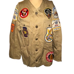 May include: A tan utility jacket with multiple embroidered patches, including "Colt", "National Champion", "NRA Expert", and "Illinois State Rifle Association".