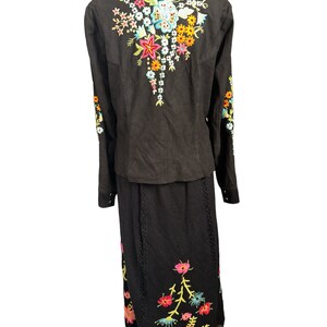 May include: Black embroidered jacket and skirt set with colorful floral designs. The jacket has a collar and long sleeves. The skirt is long and has a lace trim.
