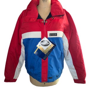 May include: A red, white, and blue ski jacket with a zipper closure and a white label that says "WOLF FORM CO. N.Y.C." on the collar. The jacket has a white tag with the text "DUPONT THERMOLOF" and "WARRANTY" on it.