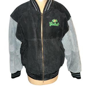 May include: A black suede bomber jacket with gray suede sleeves and a green and white embroidered logo that says "Goliath" on the front. The jacket has a zipper closure and a ribbed collar, cuffs, and waistband.