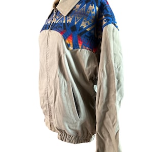 May include: A tan jacket with a zipper closure and a southwestern-style patterned fabric panel on the upper back and shoulders. The fabric panel features blue, red, orange, and brown colors.