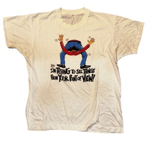 May include: A white t-shirt with a cartoon illustration of a person bending over backwards. The text on the shirt reads "I'm trying to see things from your point of view!"