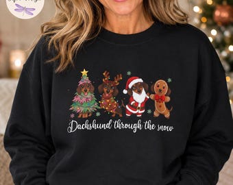 May include: A black sweatshirt featuring a graphic of four dachshunds dressed for the holidays, including one as a Christmas tree, one with reindeer antlers, one as Santa Claus, and one as a gingerbread man, with the text Dachshund through the snow.