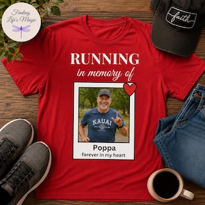 May include: A red short-sleeved t-shirt featuring the white text "RUNNING in memory of" above a rectangular photo frame containing a picture of a person wearing a blue shirt, a red heart icon, and the text "Poppa forever in my heart".
