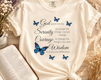 May include: A cream-colored short-sleeve t-shirt featuring a graphic print of blue butterflies and the text: God grant me the Serenity to accept the things I cannot change, Courage to change the things I can, and Wisdom to know the difference.