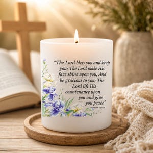 May include: A white frosted glass candle with a lit wick, featuring a floral design in shades of blue and white. The text reads: The Lord bless you and keep you; The Lord make His face shine upon you, And be gracious to you; The Lord lift His countenance upon you and give you peace. Numbers 6:24-26.