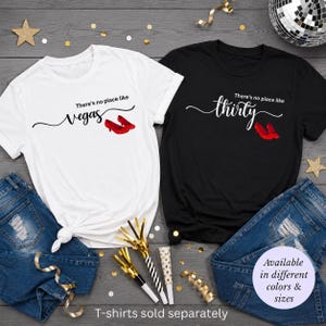 May include: Two t-shirts, one white and one black, with text and graphics. The white shirt says "There's no place like Vegas" with red high heels. The black shirt says "There's no place like thirty" with red high heels. Text at the bottom says "T-shirts sold separately."