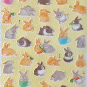 Peut inclure: Une feuille d'autocollants colorés représentant diverses illustrations de lapins mignons dans différentes poses. Les lapins sont représentés dans différentes couleurs, notamment le blanc, le brun, le gris et l'orange. Certains lapins tiennent des carottes, tandis que d'autres sont assis dans des tasses ou tiennent des fleurs. Les autocollants sont parfaits pour ajouter une touche de fantaisie aux journaux, aux planificateurs ou à tout autre projet créatif.