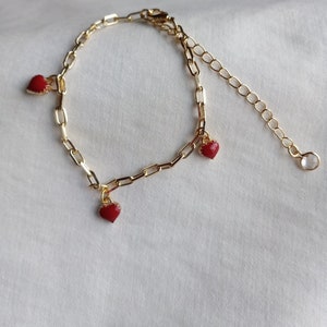 May include: A gold chain bracelet with three red heart charms. The bracelet has a lobster clasp and an extension chain.