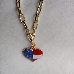 May include: A gold chain necklace with a heart-shaped pendant. The pendant is red, white, and blue and features a design resembling the American flag.