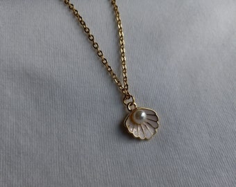 May include: A gold chain necklace with a delicate seashell pendant. The seashell is white with a pearl in the center.