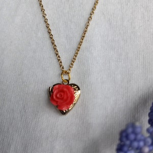 Op de afbeelding: Een gouden ketting met een hartvormige hanger met een rode roos.