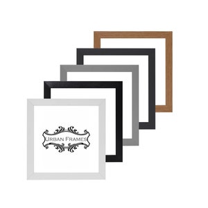 May include: Four picture frames in different colours, including white, black, grey, and brown. The frames are stacked on top of each other, with the white frame at the bottom and the brown frame at the top. The frames are all the same size and have a simple, modern design. The text "URBAN FRAMES" is printed on the white frame.