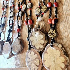 Può includere: Più fili di collane realizzate con perline nere, rosse e bianche, con grandi ciondoli marroni a forma di fiore.