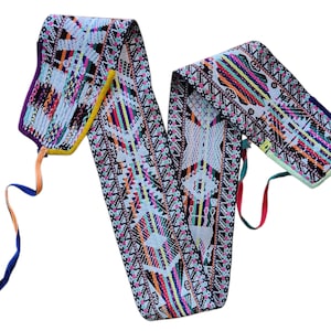 May include: A colorful, intricately woven textile belt with a white base and geometric patterns in shades of pink, orange, green, yellow, and blue. The belt has long, decorative ribbons in various colors attached to the ends.