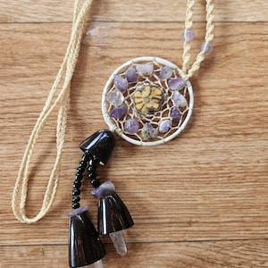 Può includere: Una collana con ciondolo a forma di acchiappasogni bianco con cristalli di ametista e quarzo trasparente, un pendente di perline di legno marrone e un cordoncino beige.