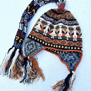 May include: A colorful knitted hat with a long tassel and ear flaps. The hat features a geometric pattern with figures holding hands.