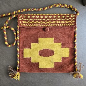 May include: A woven shoulder bag in shades of brown and yellow. The bag features a geometric design in yellow on the front, with a flap closure and a braided strap. Tassels adorn the bottom corners.