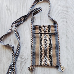 Peut inclure: Un sac bandoulière rectangulaire en tissu tissé avec un motif géométrique dans des tons marron, noir, blanc et gris. Le sac comprend une longue bandoulière assortie, un compartiment principal zippé, une poche avant zippée et des petits pompons.